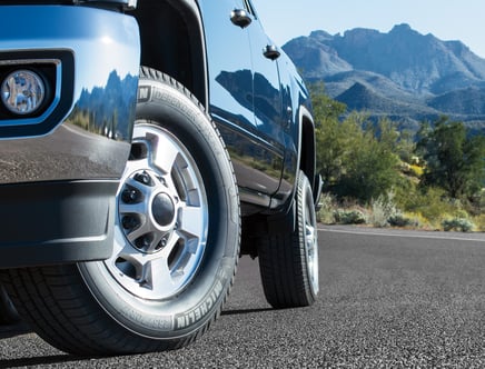 Close-up of the front tire of a blue truck on a paved road with mountains in the background.