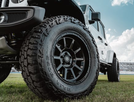 Close-up of an off-road tire on a white vehicle parked on grass under a partly cloudy sky.