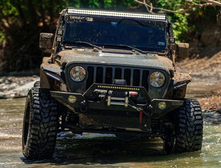 A muddy off-road vehicle with large tires and additional lights driving through water.