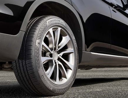 Close-up of a car tire with Kumho branding, mounted on a sleek black vehicle.