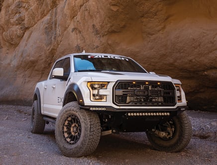 White off-road truck parked near a rocky cliff.