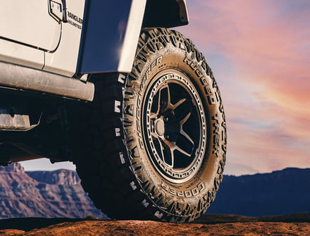 Close-up of an off-road vehicle tire on rocky terrain with a scenic desert landscape in the background.