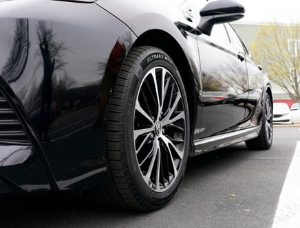 Low-angle view of a black car with reflective paint, featuring a close-up of the front wheel and tire.