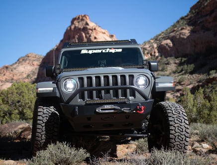 A rugged off-road vehicle with large tires navigates a rocky desert landscape under a clear blue sky.