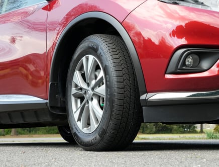 Close-up of a red car's front tire and wheel on a paved surface.