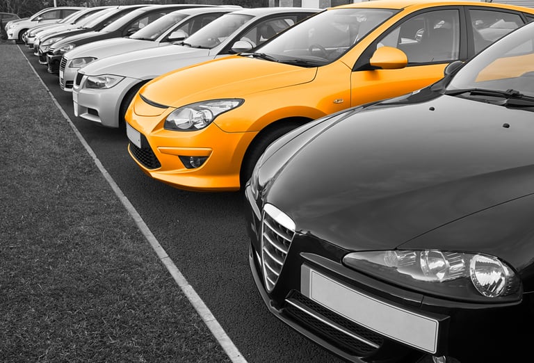 A row of cars parked side by side, featuring a distinctly colored yellow car among mostly black and white vehicles.