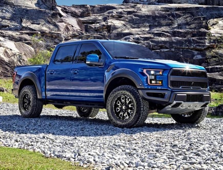 Blue pickup truck parked on gravel in front of rocky terrain.