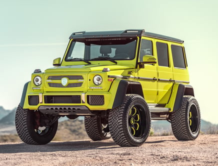 Bright yellow SUV with matte black trim parked on dirt, featuring large tires and off-road enhancements.