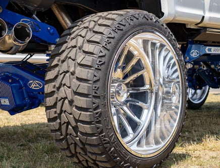 Close-up of a large off-road tire with a shiny chrome rim on a lifted truck with blue suspension.