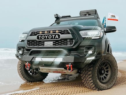 Black Toyota truck with off-road modifications parked on sandy beach.