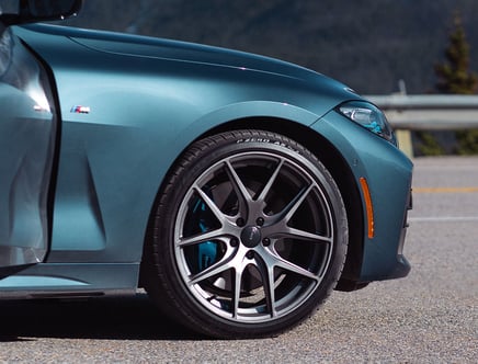 Front wheel and fender of a teal sports car with visible brake caliper and tire branding.