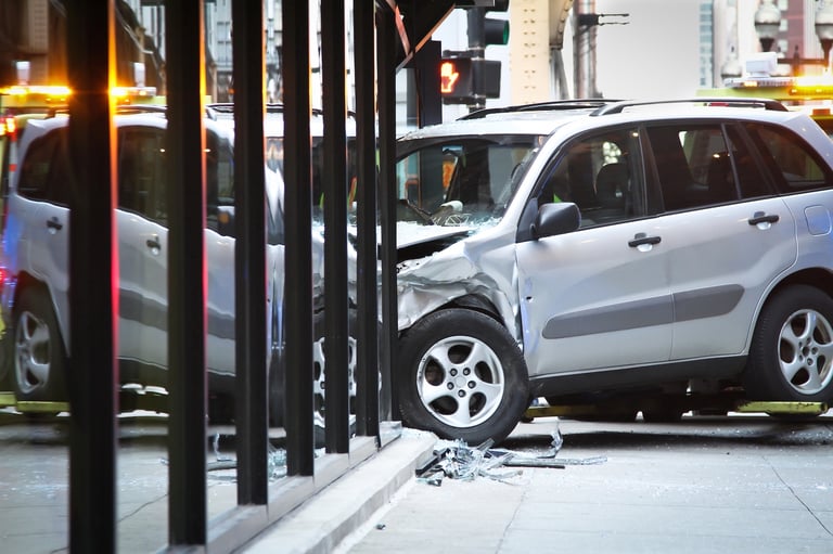 Silver SUV crashed into a storefront window with visible damage and glass debris on the sidewalk.