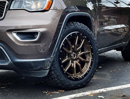 Close-up of a Jeep Grand Cherokee with bronze aftermarket wheels on a wet pavement.