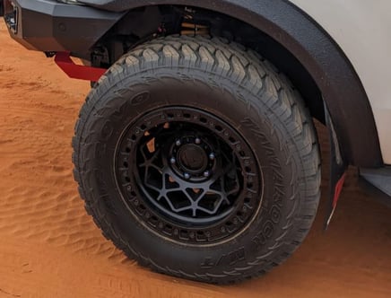 A close-up of a vehicle's off-road tire on sandy terrain.