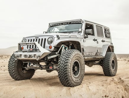 A heavily modified off-road Jeep with large tires and custom bumpers parked on a sandy terrain.