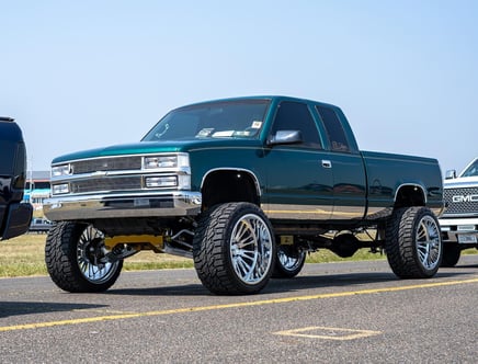 A lifted dark green pickup truck with large chrome wheels parked in a lot.