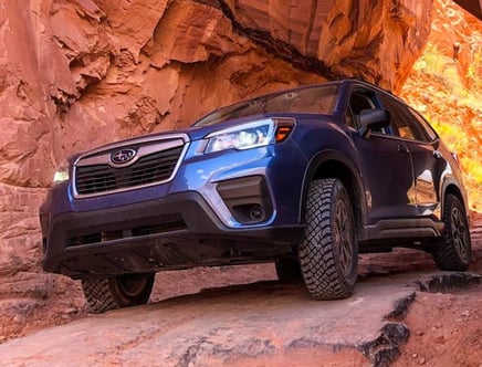 Blue SUV driving on a rocky terrain under a red rock arch.