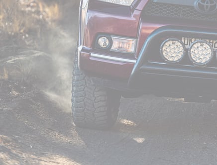 Close-up of a red off-road vehicle driving on a dirt path, kicking up dust with its front tire.