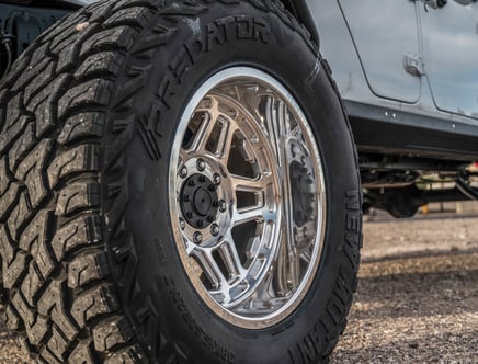 Close-up of an off-road vehicle's tire with a rugged tread pattern and shiny metal rim.