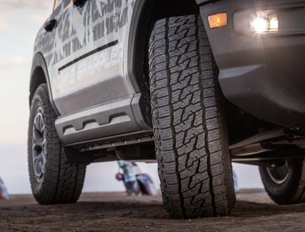 A close-up view of an off-road vehicle's front tire on a dirt surface, showcasing the tread pattern.