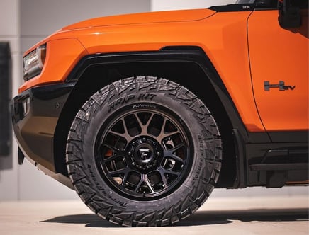 Close-up of an orange vehicle's front section and tire with off-road tread.