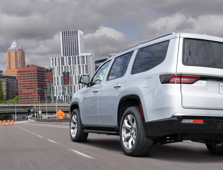 Silver SUV driving on a city road with tall buildings in the background.