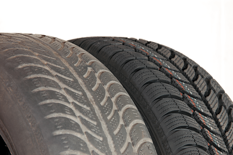 Closeup of a bald tire on the left and a brand new tire on the right. Same make model.