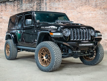 Black Jeep Rubicon with bronze rims parked in front of a brick wall.